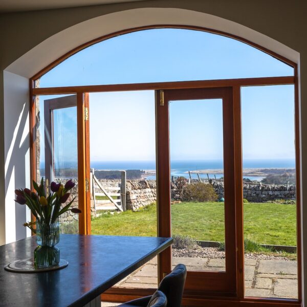 Interior of kitchen with island and patio doors opened over garden with views over Loch Fleet at Balvraid Steading, near Dornoch