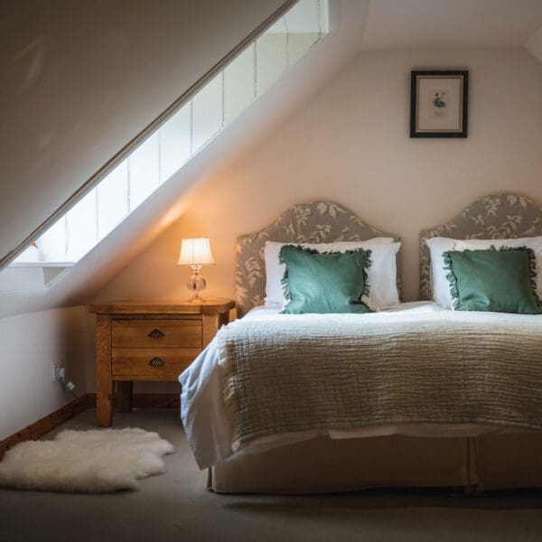 Double bed with green cushions and lit bedside lamps in Grieve's Cottage, Skelbo Dornoch