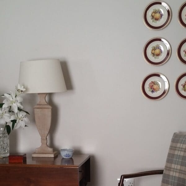 Living room interior of Gleann Gollaidh, Dornoch with lamp and flowers on table, tartan chair and plates on wall