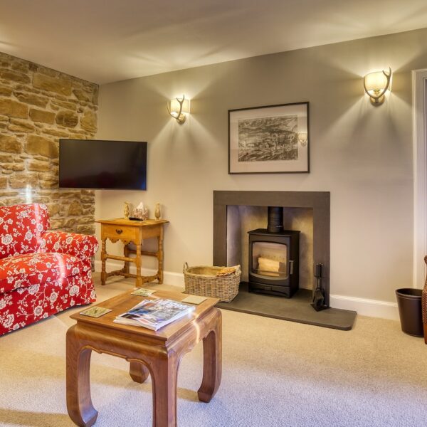 Living room with wood burning stove, red couch and exposed stone feature wall in The Meadows, Dornoch