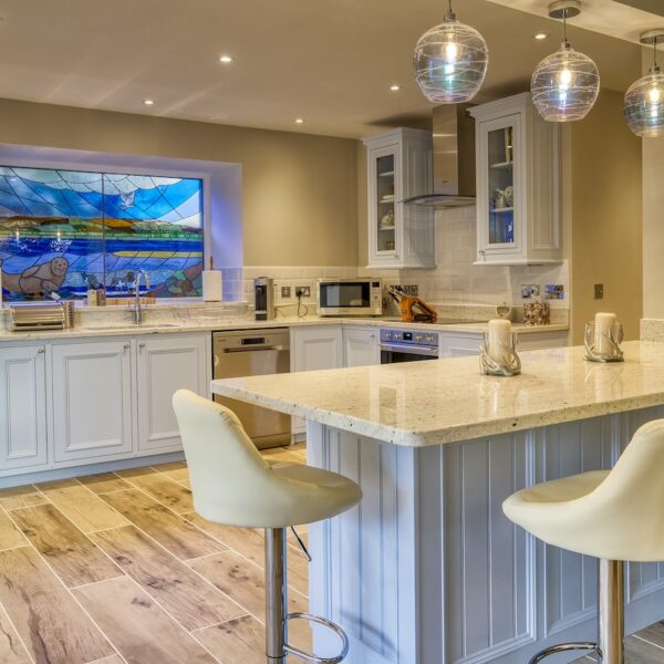 Open plan kitchen with breakfast bar, light blue cupboards and stained glass window in The Meadows, Dornoch