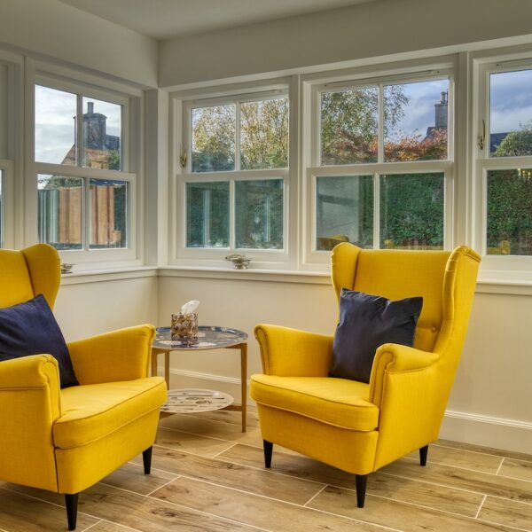 Sitting area with windows looking over garden and two bright yellow armchairs in The Meadows, Dornoch