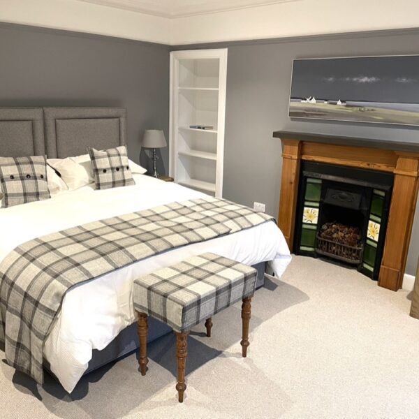 Double bedroom with grey decor, wooden fire surround and bed with grey tartan cushions and throw in 2 Quail, Dornoch