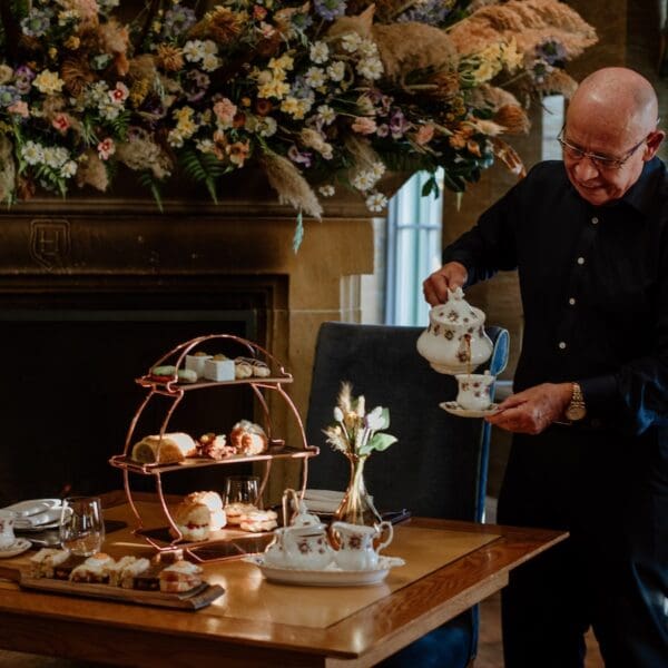 Waiter pouring tea at table set with afternoon tea items, Links House Hotel Dornoch