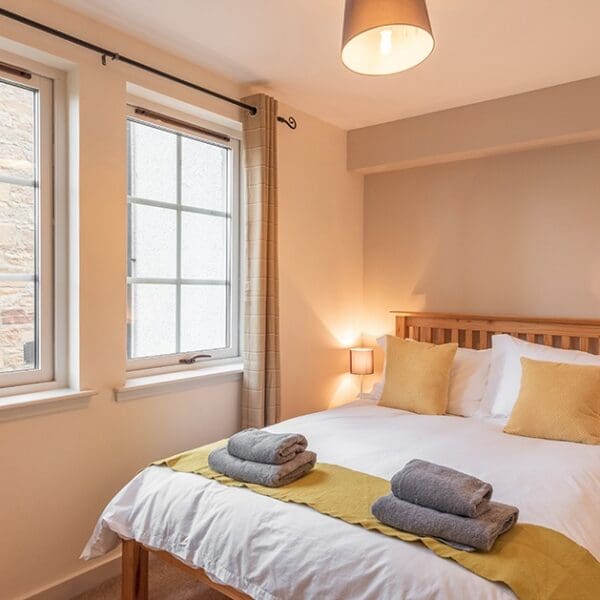 Double bedroom with pine bed, yellow cushions and throw on white bed linen and bright windows in Dornoch Mews, Dornoch, Highlands