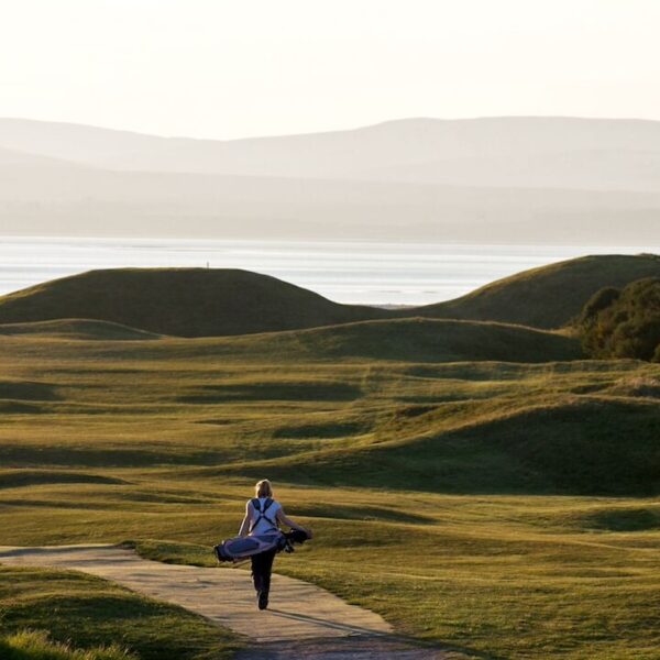 Rear view of female golfer carrying golf bag walking along path on Tain Golf Club, Tain Highlands