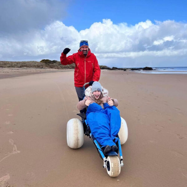 Girl in wheelchair and her dad on Dornoch Beach