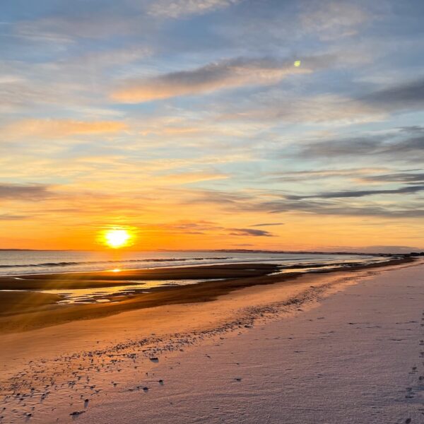 Low winter sun at Embo beach with footprints through frost on sand