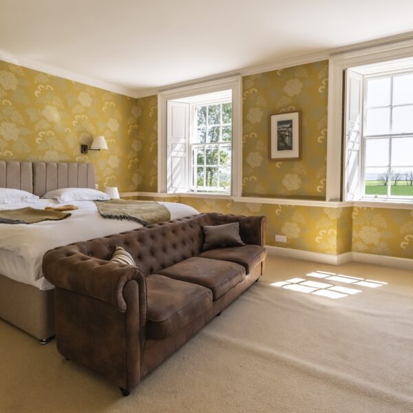 Bedroom in Embo House, Dornoch with dark yellow wallpaper and brown leather couch