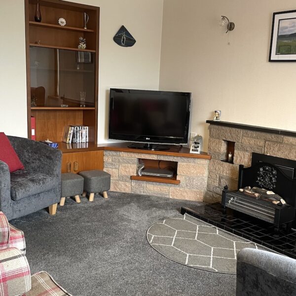 Living room of Oystercatcher, Gate Street, Embo with tv and fireplace, grey carpet and red and grey furniture