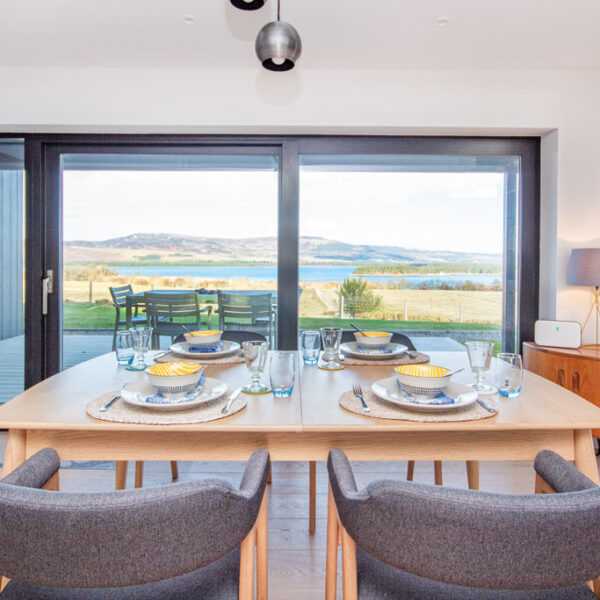 Dining table with grey chairs next to patio doors out to decking and view north over Loch Fleet, Oran Mor, self catering house in Skelbo, Dornoch