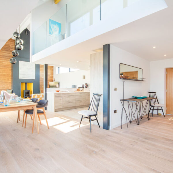 Open plan living, kitchen, dining space with light wood flooring and grey and yellow accent colours, cathedral ceiling and glass panelled balcony Oran Mor, self catering house in Skelbo, Dornoch