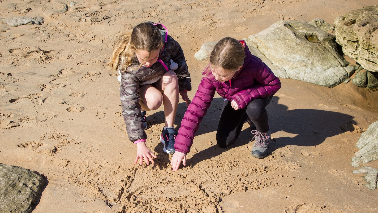 two girls drawing pattern in sand on Dornoch beach