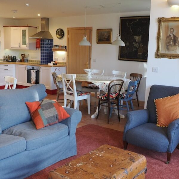 Open plan area of The Curling Pond, Dornoch with white kitchen cabinets, dining table and blue couch and chair