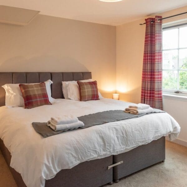 Double bedroom with grey bed and red tartan cushions and curtains in Dornoch Mews, Dornoch, Highlands